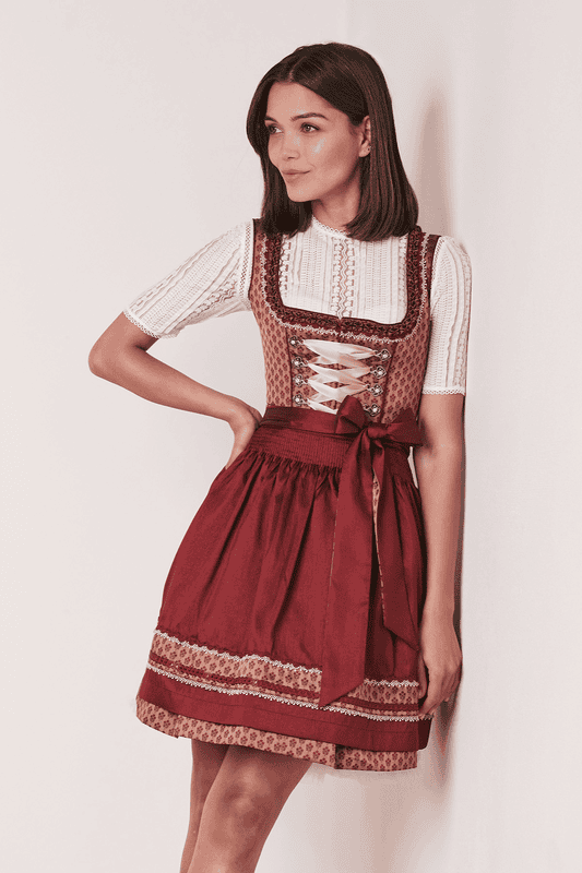 Das Dirndl Alica bezaubert durch klassische Miederhaken und feine Borten entlang des Mieders. Eine Dirndlschürze in Wildseidenoptik vervollständigt den Look.